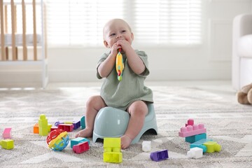 Cute little baby with toy sitting on potty at home