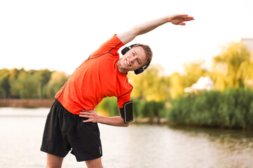 Smiling sportsman in headphones and armband doing morning exercise near river