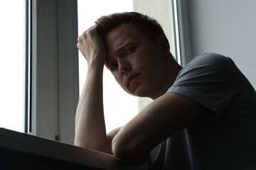 Sad thoughtful man near window indoors, low angle view. Depression