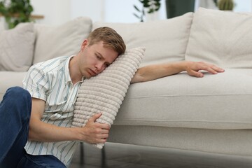 Sad tired man with pillow leaning on sofa at home