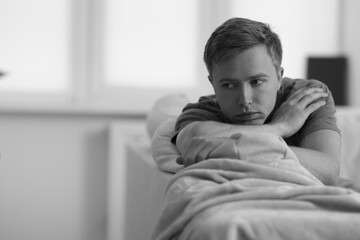 Sad thoughtful man on sofa at home, space for text. Black and white effect
