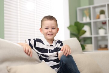 Cute little boy laughing on sofa at home
