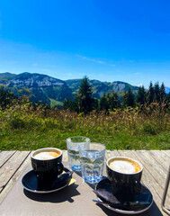 Summit serenade: two steaming cappuccinos amid alpine panorama, evoking Transhumance and Alpine...