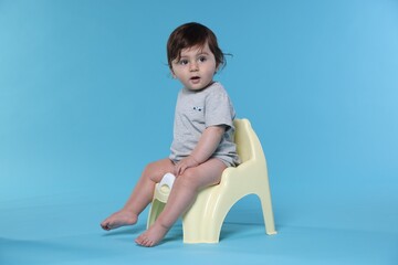 Cute little baby sitting on potty against light blue background