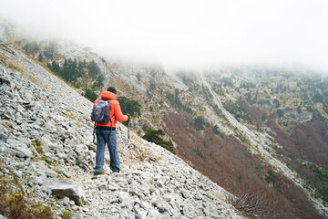 Tourist walking narrow trail across scree slope in Komovi mountains during foggy autumn day. Themes...