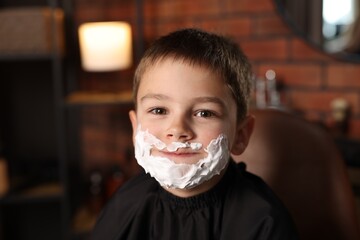 Little boy with shaving foam on his face in barbershop