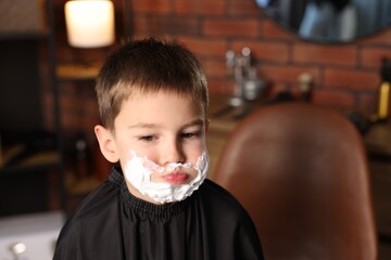 Little boy with shaving foam on his face in barbershop