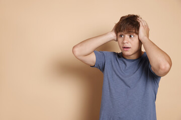 Teenage boy suffering from panic attack on beige background. Space for text