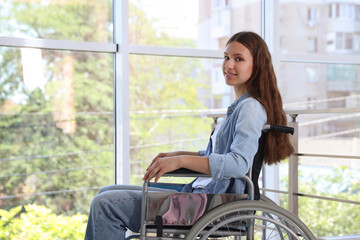 Smiling teenage girl in wheelchair near window indoors