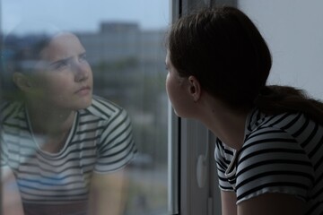 Sad young woman near window at home, space for text