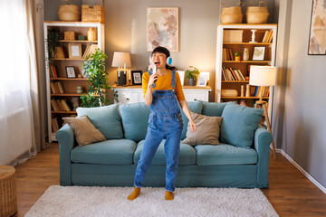 Obraz premium Woman having fun listening to the music, singing and dancing while relaxing at home