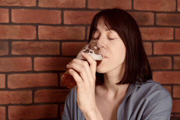 Young woman drinking beer near brick wall in bar