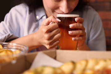 Young woman drinking beer at table with food in bar, closeup