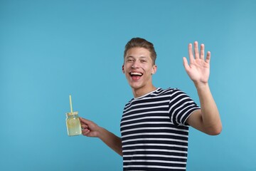 Happy man with mason jar of lemonade on light blue background. Refreshing drink