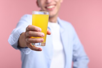 Happy man with glass of orange juice on pink background, closeup. Refreshing drink