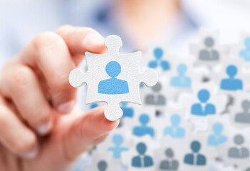 Close-up of hands holding a jigsaw puzzle piece with a blue avatar icon on it, surrounded by many other people's avatars in a grey color