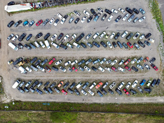 Drone aerial view image of a vehicle scrap yard showing rows of damaged and end-of-life cars,...