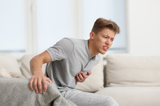 Young man suffering from chest pain on sofa at home