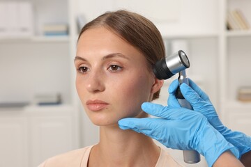 Doctor examining young woman's mole with dermatoscope in hospital