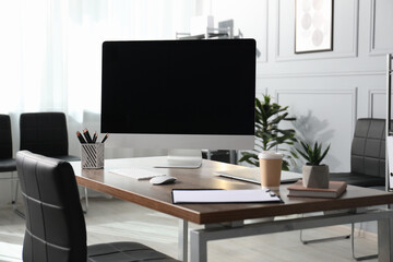 Stylish workplace with modern computer, laptop, stationery, coffee and floral decor on wooden table in office