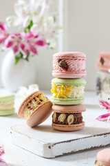 Colorful macarons stacked on a wooden board, surrounded by fresh flowers in a bright kitchen setting