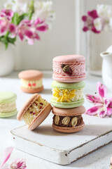 Colorful macarons stacked on a white wooden board with floral decorations in the background during a bright afternoon