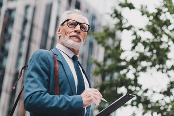 Confident senior businessman in blue suit with clipboard outdoors in urban cityscape