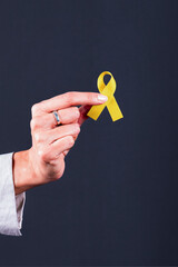 Woman’s hand holding a yellow ribbon, symbol of bladder cancer, endometriosis, and suicide...
