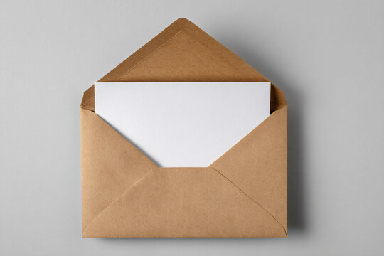 Blank white invitation or greeting card mockup in an open brown recycled kraft paper envelope