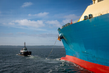 Tug boat assisting big cargo ship. Large cargo ship enters the port escorted by tugboat.