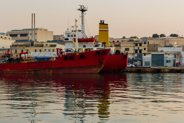 Two Red Cargo Ships Docked in an Urban Harbor at Sunset