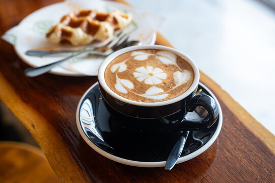 Hot coffee latte with latte art milk foam in cup mug and Homemade Belgian Waffles with honey on wood desk on top view. As breakfast In a coffee shop at the cafe,during business work.