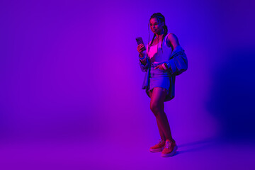 Stylish young woman holding a phone in neon lighting, wearing denim and colorful outfit, exuding casual modern vibes