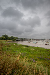 River Deben at low tide with small boats under a stormy sky. View towards the historic town of Woodbridge in Suffolk, UK.
