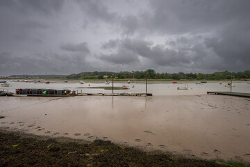 River Deben at low tide with small boats under a stormy sky. View across the river near the historic town of Woodbridge in Suffolk, UK.