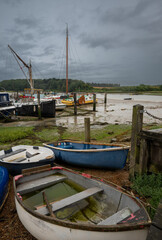 Small boats under a stormy sky. View of the quay at low tide on the River Deben in the historic town of Woodbridge in Suffolk, UK.