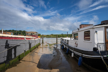 Boats sitting on mud in sunshine. View of the quay at low tide on the River Deben in the historic town of Woodbridge in Suffolk, UK.