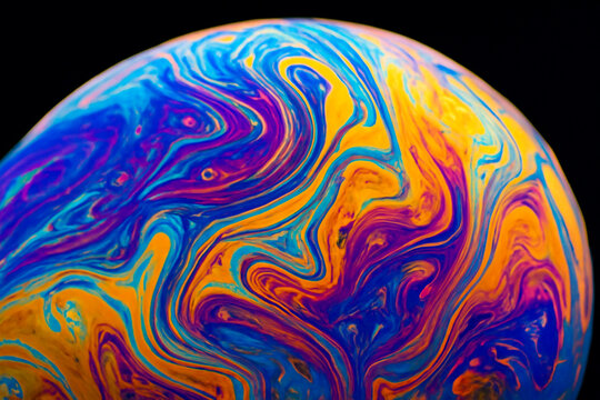 Vibrant abstract macro of soap film surface with swirling rainbow colors and fluid patterns on black background