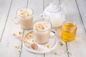Calming natural chamomile flowers tea latte, organic late night cozy warm beverage with milk and floral chamomile tea, with honey and ginger spices
