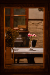 Romantic restaurant table with pink gerbera flowers, viewed through a wooden window frame creating a cozy, intimate atmosphere.