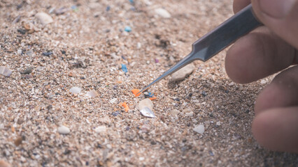 Scientific research on beach pollutants: A macro photograph shows tweezers meticulously separating a single microplastic fragment from the sand, symbolizing the detailed investigation into environment