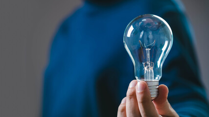 A person holding a light bulb, symbolizing ideas, innovation, and creativity, set against a blurred background.