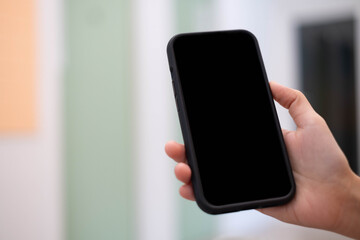 A hand holding a smartphone with a blank screen, set against a softly blurred background.