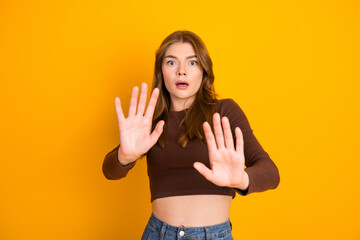 Young woman with long brown hair reacting emotionally, standing against a vibrant yellow...