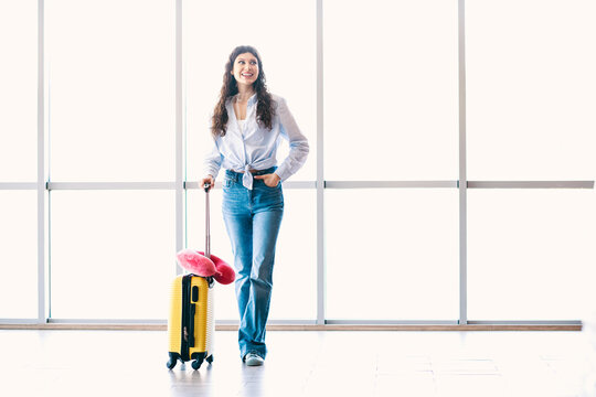 Smiling woman with yellow suitcase enjoying her journey at an airport terminal and ready for a new adventure