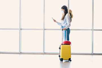 Charming woman at an airport terminal, holding a yellow suitcase and using her phone, ready for a...
