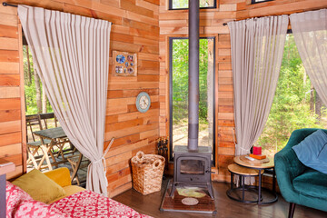 A cozy wooden cabin interior featuring a stove, comfortable seating, and spacious windows framing a...