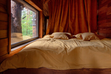A cozy wooden bedroom with yellow bedding, curtains, and a window offering a serene forest view....