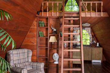 Charming wooden attic interior with a ladder accessing a loft, armchair, and rustic decor. Snug...