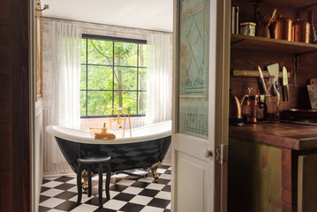 A beautifully designed bathroom features a black clawfoot bathtub with natural light streaming...